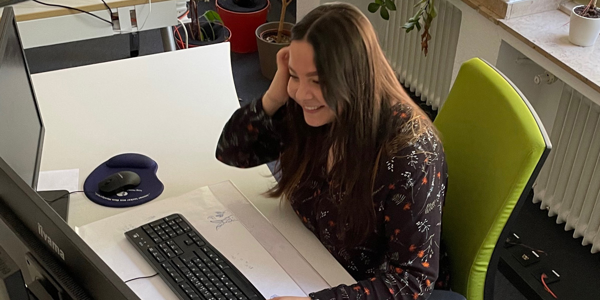 Lächelnde Frau, während sie in einem Büro an einem Schreibtisch mit Computer und Tastatur arbeitet.