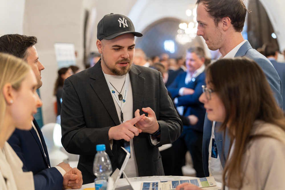 Vier Personen in Geschäftskleidung unterhalten sich bei einer geschäftigen Networking-Veranstaltung an einem Tisch.